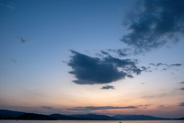 Fluffy grey cloud meets calm multicolor sea. Moored boat in sea water. Mountain background, space.