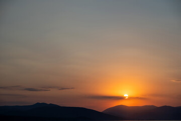 Sunset over mountain silhouette on colorful sky background. Golden sun hides behind cloud. Space