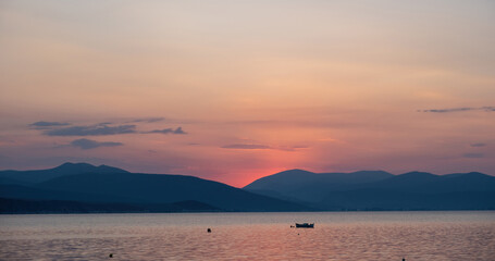 Obraz premium Colorful sky pink purple color over sea water. Mountain silhouette, moored boat in open Greek sea.