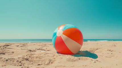 Obraz premium Brightly colored beach ball on a sunny sandy beach with a clear blue sky, perfect for summer fun and relaxation.