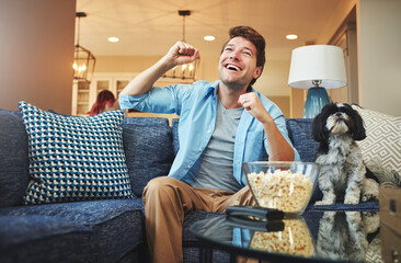 Excited, man and celebration with watching tv or popcorn in home on sofa with sports game, challenge and fun. Living room, couch and smile or happy with fist with dog for win, tournament or support