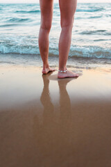 Summer mood. Back view. woman stands in the sea. legs close up. The foam of sea water washes the sand and the feet of a young beautiful girl at sunset. .