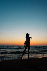Fototapeta premium girl enjoying a walk on the beach at sunset. Silhouette of a woman looking at the sunset. Summer mood.