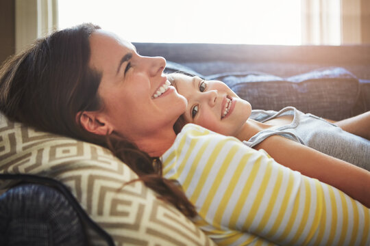 Love, smile and mother cuddle her child while relaxing on sofa in the living room of their home. Happiness, bonding and young mom embracing and her laughing daughter with care in their family house