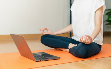 Woman sitting on floor in lotus pose and meditating while practicing yoga in home.