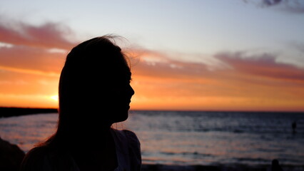 Fototapeta premium Head and shoulders, silhouette of young woman a sunset. Beautiful orange colors. Copy space