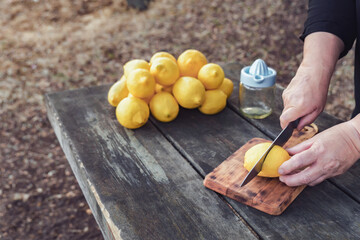 a woman cuts fresh lemons with a knife on a wooden table in the field with a pile of lemons and a...