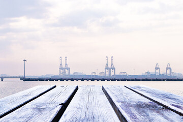 Naklejka premium Empty wooden planks or brown table floor. With port, cranes lift containers and fog covers orange sky and white clouds in morning. Abstract texture background. For place food, drink.