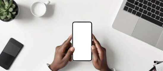 A person is holding a cell phone on a table with a laptop and a cup