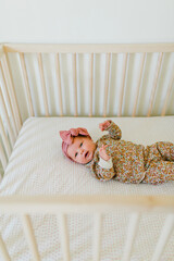 Newborn baby girl lays in floral onesie in wooden crib