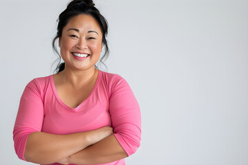 Beautiful and healthy Asian American female, smiling while wearing a pink workout outfit, is standing in front of a white background, conveying the importance of having a healthy lifestyle.