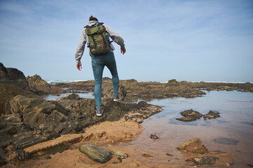 Young adventurer exploring rocky coastline with a backpack on a sunny day