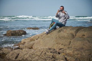 Man taking photos with smartphone on rocky shore by the ocean