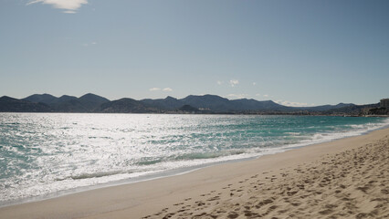Clear blue waves with strong wind on a sandy empty beach in Cannes with Theoule-sur-Mer on background