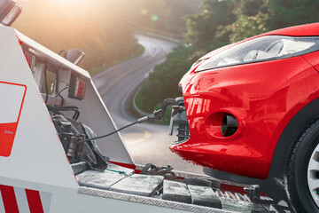 Close-up of a red car being towed by a tow truck on a rainy day with a winding road in the background.