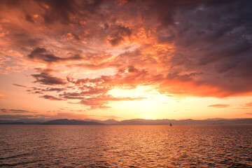 A traditional three mast ship silhouetted against a beautiful golden sunrise over the rugged coastline of the island of Corsica as it lights up the Mediterranean sea