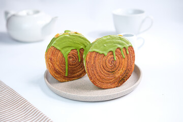 Cromboloni or round puff pastry filled with cream, and glazed with matcha topping. 