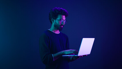 Arabian Indian man guy male programmer coder internet computer developer businessman business guy gamer hold laptop computer invite come here welcome nod head invitation work in violet neon background © Yuliia