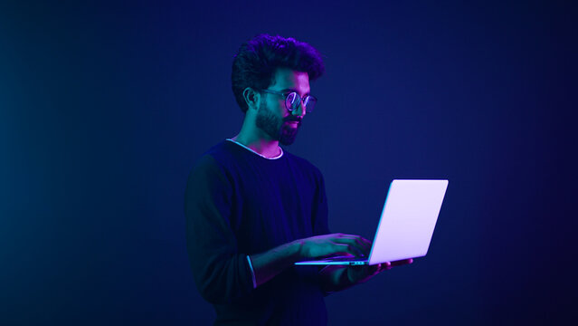 Arabian Indian man guy male programmer coder internet computer developer businessman business guy gamer hold laptop computer invite come here welcome nod head invitation work in violet neon background