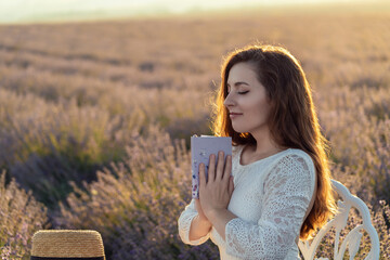 A woman is sitting in a field of lavender flowers, holding a book in her lap. She is in a peaceful...
