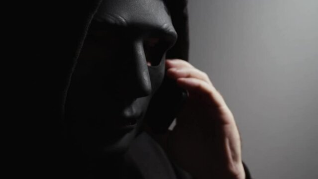 Phone Scammers, man in a mask with a phone, phishing and hacking, fraudulent calls to steal passwords, spy on mobile devices.