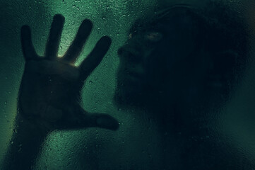 Horror scene of a man against wet glass. Hand against the background of a wet glass bathroom wall....