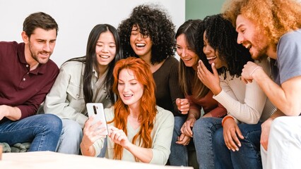 Happy woman showing smartphone to cheerful diverse friends in living room at home