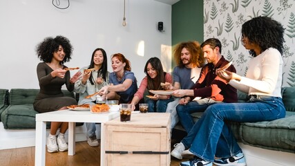 Diverse friends holding delicious pizza slices in living room during weekend party
