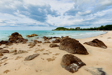 Beach with smooth, golden sand and smooth rocks scattered along the shore with cloudy sky