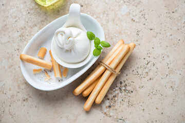 Burrata with grissini or italian bread sticks on a beige granite background, horizontal shot with space, high angle view