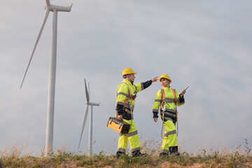 engineer with turbine. Engineers windmill team wearing uniform and helmet walking survey work in wind farms after inspection and maintenance of wind turbine to generate electrical energy.