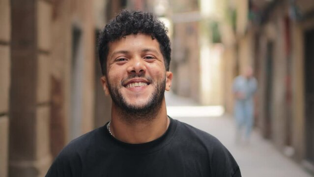 Close up individual portrait of one arab male smiling and looking at camera outside. Young adult arabic guy staring front and laughing with friendly expression. Joyful man with carefree attitude
