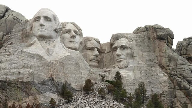 Mount Rushmore sculpted heads of George Washington, Thomas Jefferson, Theodore Roosevelt and Abraham Lincoln. Overcast sky over the intricately carved faces of this iconic American monument.