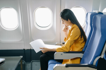 Young Asian executive excels in first class, multitasking with digital tablet, laptop and...
