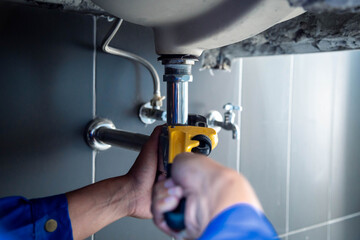 Plumber fixing white sink pipe with adjustable wrench.