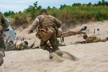 WWII  Historical reconstruction. An American medic during a battle on the beach. View from the back.