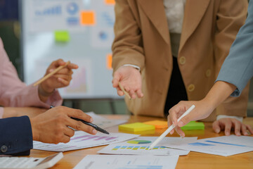 Close-up of diverse businesspeople gathering at the office desk to discuss company financial paperwork at a meeting together, multiracial colleagues brainstorm work with documents at an office.