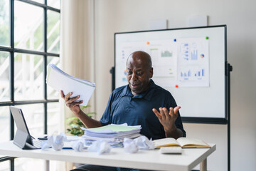 Frustrated Businessman Working at Desk with Crumpled Papers and Documents in Modern Office Setting
