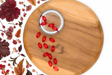 Red capsules and tablets of vitamins and medicinal herbs in beautiful textured wooden tray on white background