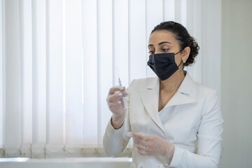 A medical professional in a mask attentively examines a syringe, ensuring safety and accuracy in...