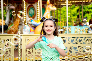 Fototapeta premium A child girl in an amusement and amusement park inflates soap bubbles in summer, International Children's Day, happy childhood and holidays