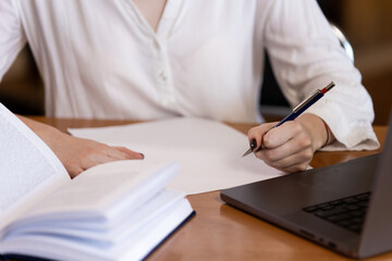 A teenage girl in the library writes an essay or a note, takes notes, prepares for an exam. Study and education concept.