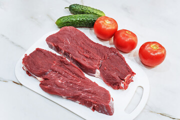 Raw veal steak with tomatoes and cucumbers on white natural marble table