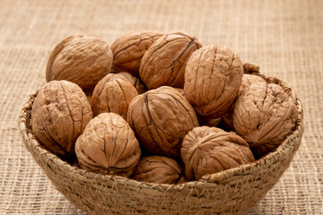 Close-up view of a wicker bowl full of shelled walnuts on a wooden surface