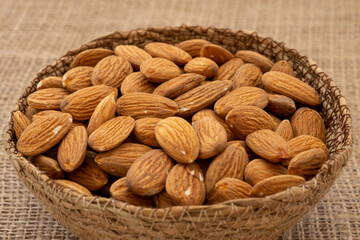 Close-up view of a wicker bowl full of roasted and peeled almonds on a wooden surface