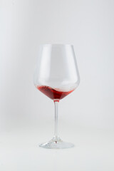 Half-full wine glass with red wine, set against a white background. The elegant swirl of wine highlights its rich color, making it perfect for themes related to wine, beverages, and fine dining.