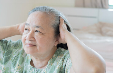 A senior woman suffers from a headache after wake up in the morning and she is holding her head in her hands.