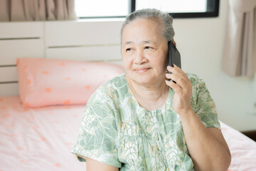 Close up portrait of an old Asian woman happily using her smart phone with her family in bedroom