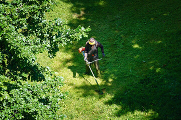 Worker trimming grass, aerial view. Worker mowing lawn in residential area, cutting and...