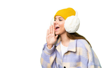 Young blonde woman wearing winter muffs over isolated chroma key background shouting with mouth wide open to the lateral